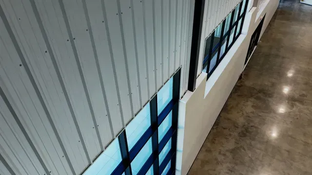 High-angle view of a building interior with vertical corrugated metal walls, large glass windows, and a concrete floor.