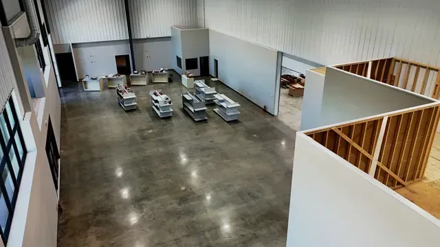 An elevated view of a warehouse-style interior with polished concrete floors, work stations, and framing for a new room.