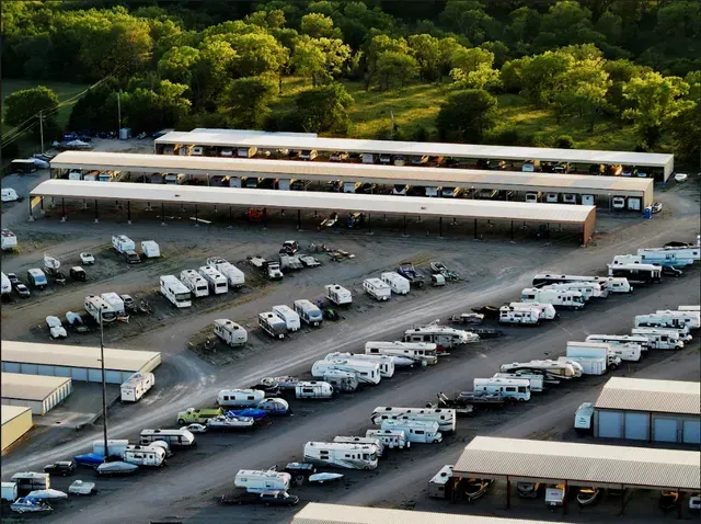 An aerial view of a large outdoor RV and boat storage facility with several long covered shelters and many parked vehicles.