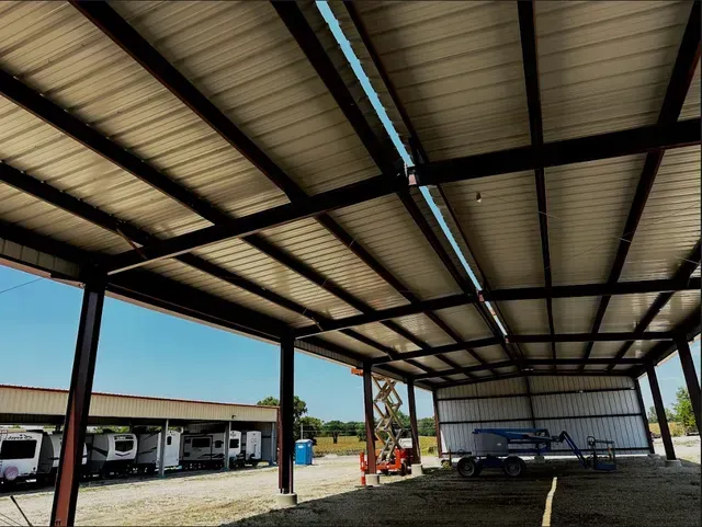 A wide-angle view of a large, open-air metal storage canopy with RVs parked under a smaller adjacent structure.