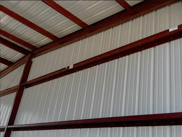 Interior view of a metal building with white corrugated wall and roof panels attached to reddish-brown steel support beams.