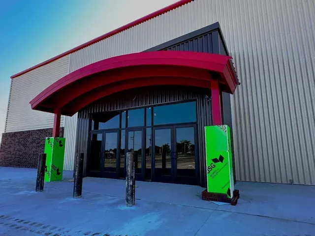 Entrance to a metal building with a curved red awning, dark glass doors, and bright green protective foam on pillars.