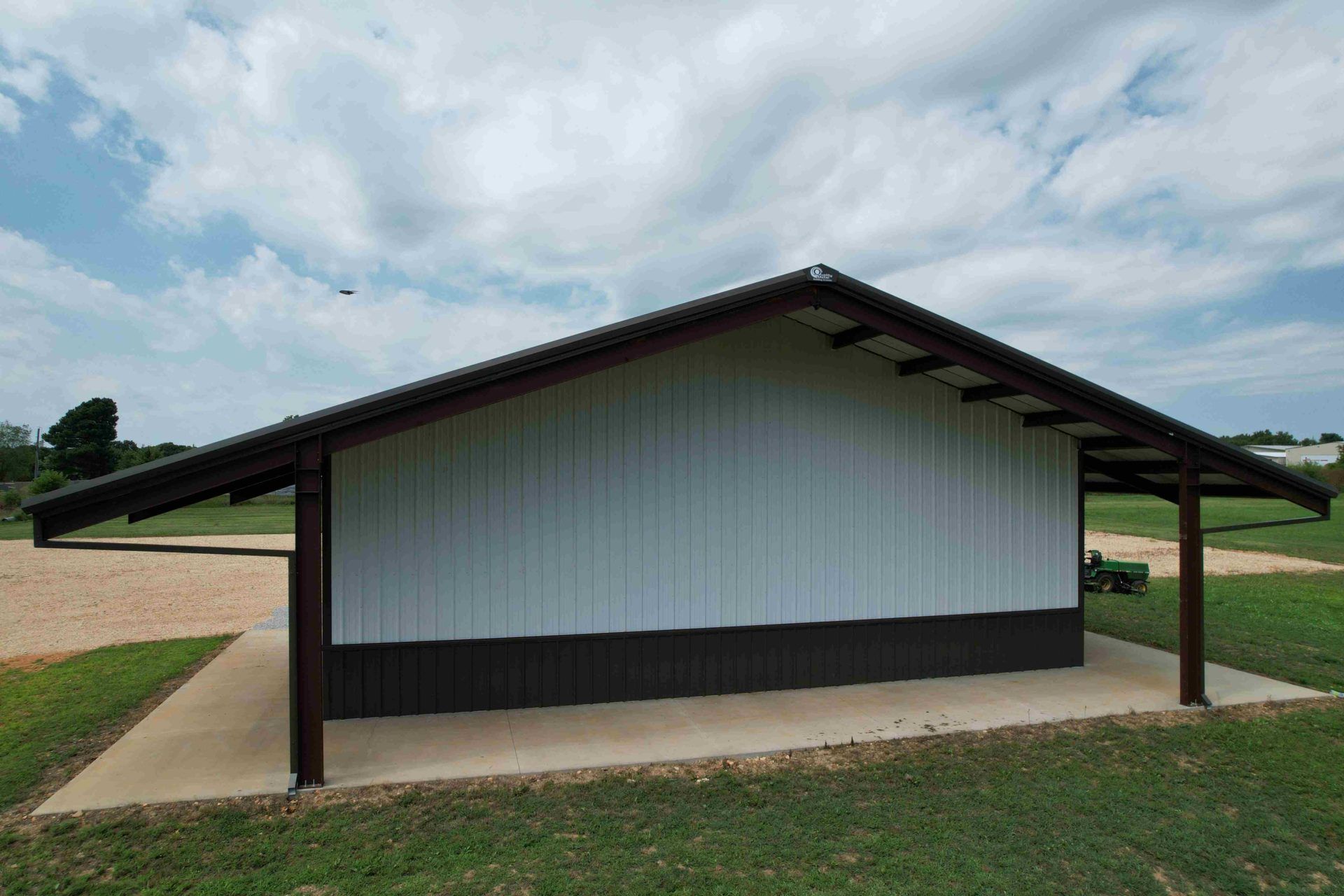 l building shelter with brown roof, support beams, and white and brown walls on a concrete slab
