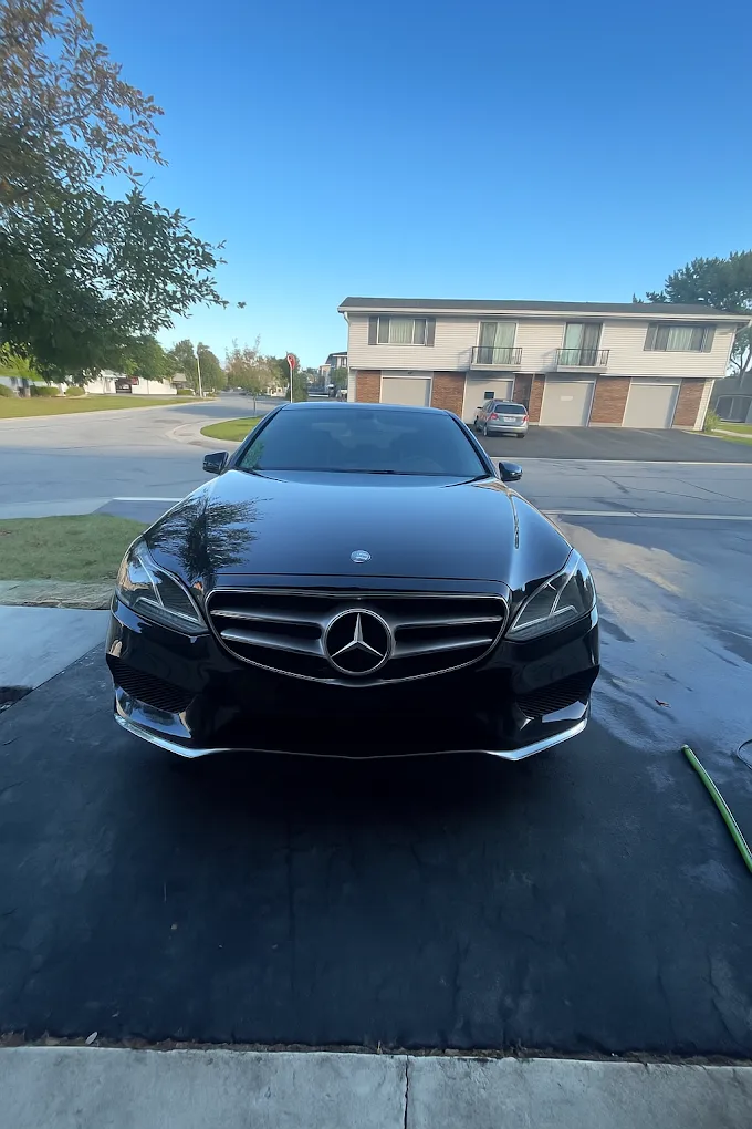 Black Mercedes sedan parked in a driveway on a sunny day, with a house and trees in the background