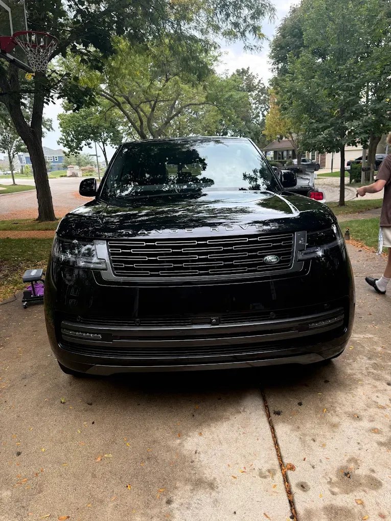 Black SUV parked on a tree-lined street, front view on a sidewalk.
