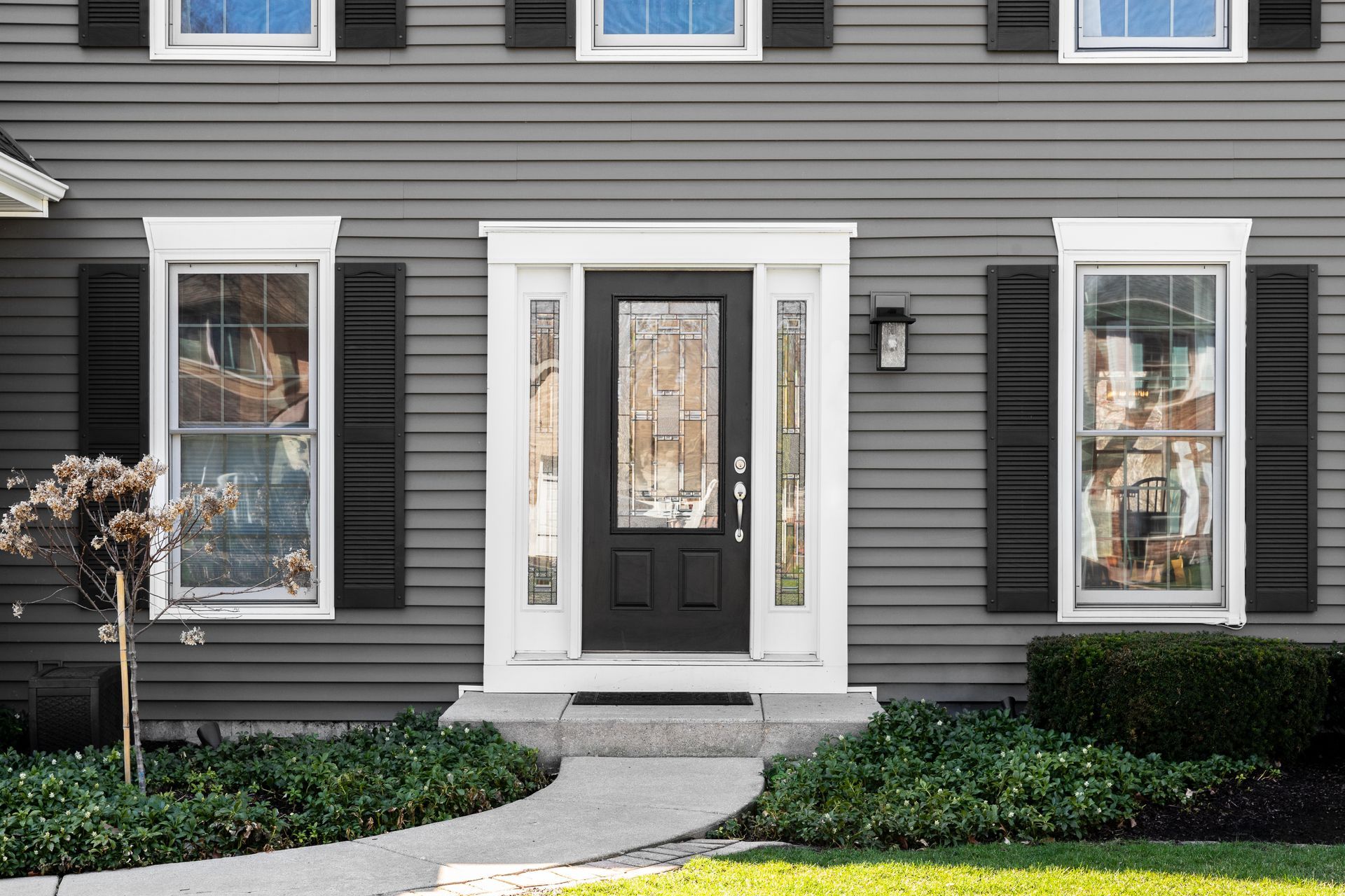 Front entrance of a gray house with black shutters, white trim, and a black door beside a curved walkway. Front entrance of a gray house with black shutters, white trim, and a black door beside a curved walkway.