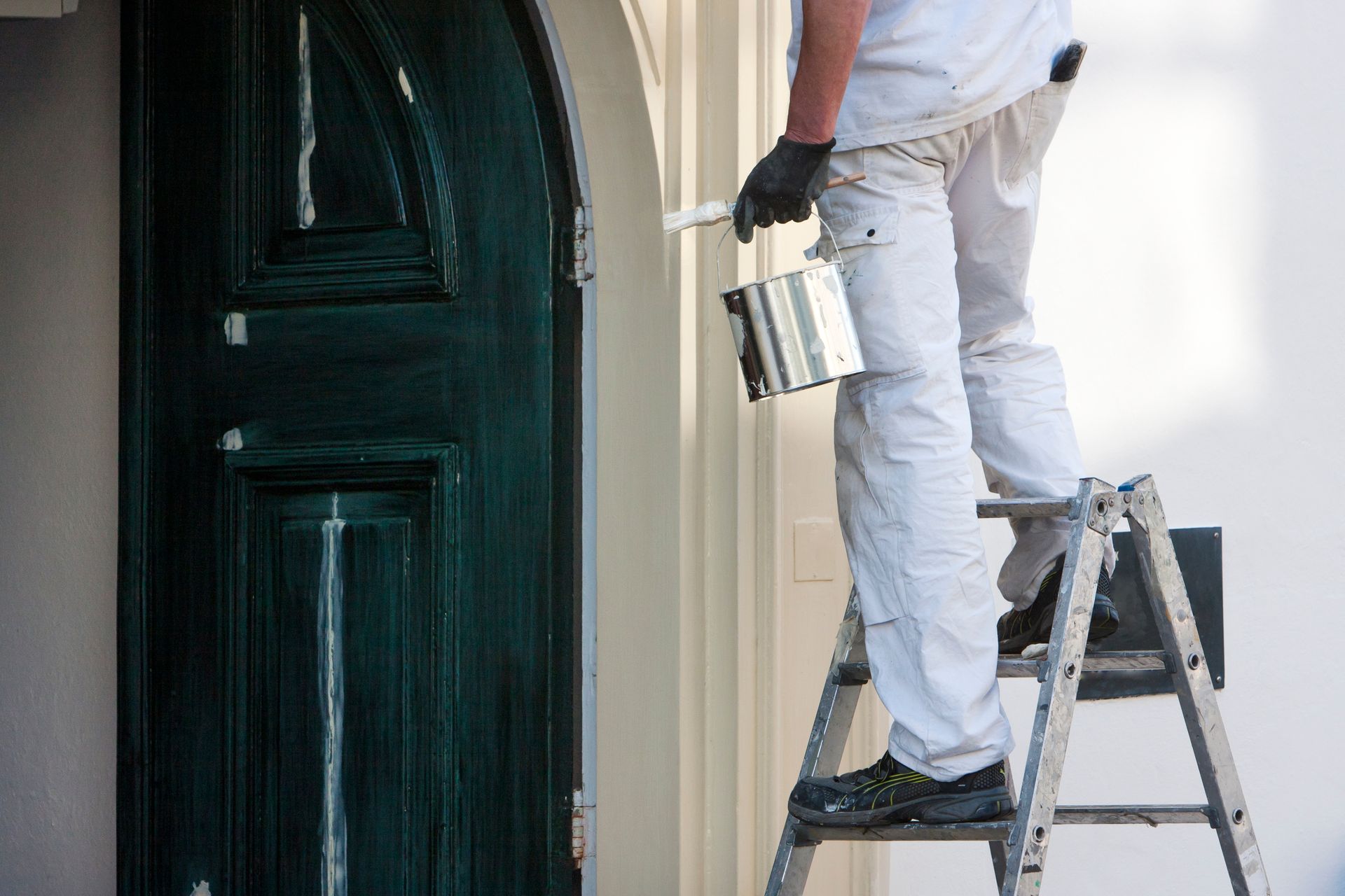 Person painting an exterior door while standing on a ladder, holding a paint can Person painting an exterior door while standing on a ladder, holding a paint can
