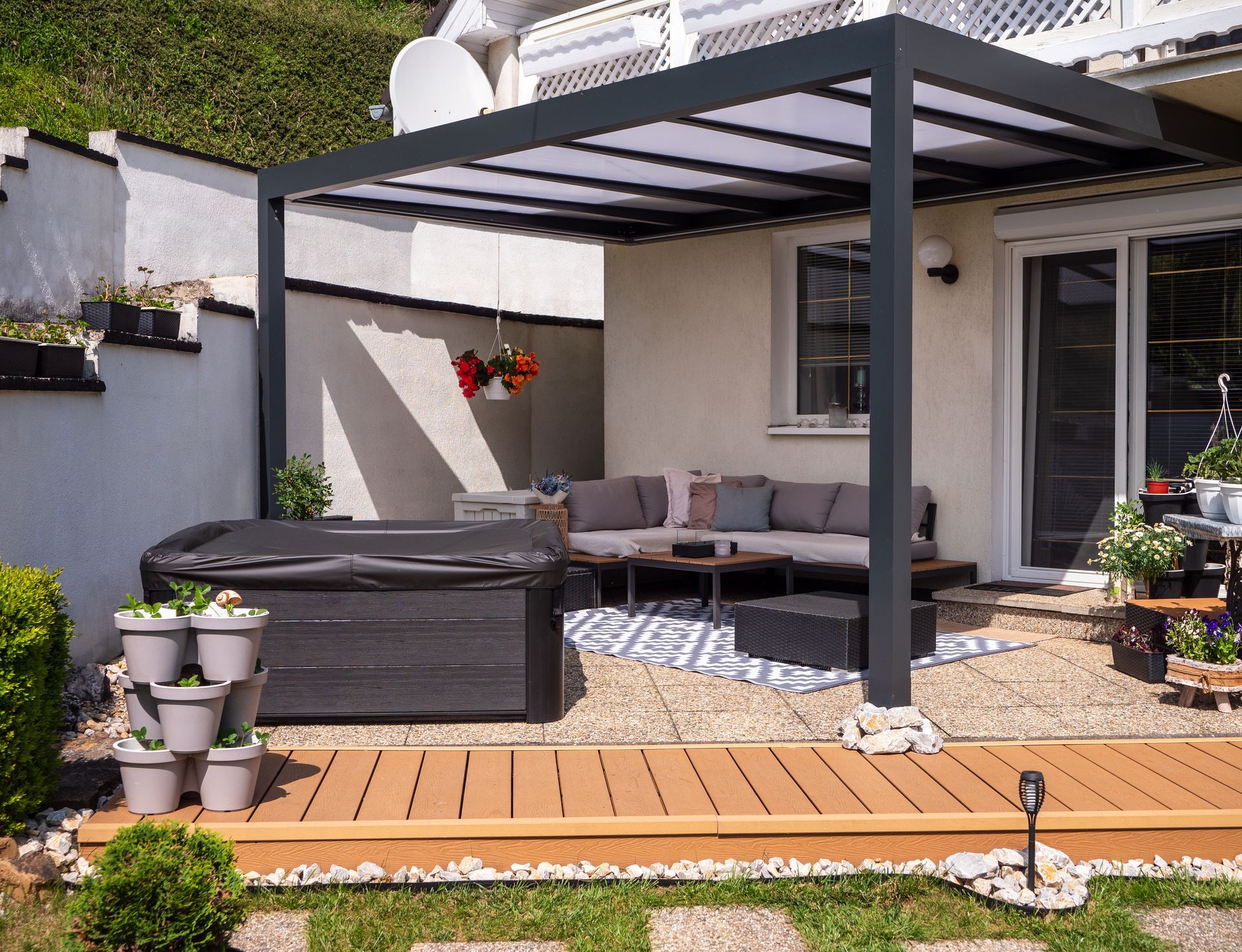 Patio with gray pergola, outdoor sofa, and potted plants beside a house Patio with gray pergola, outdoor sofa, and potted plants beside a house