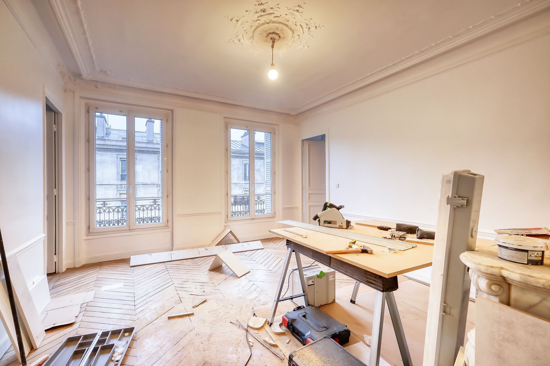 Bright, unfinished room with white walls, large windows, and construction tools on the floor and a workbench. Bright, unfinished room with white walls, large windows, and construction tools on the floor and a workbench.