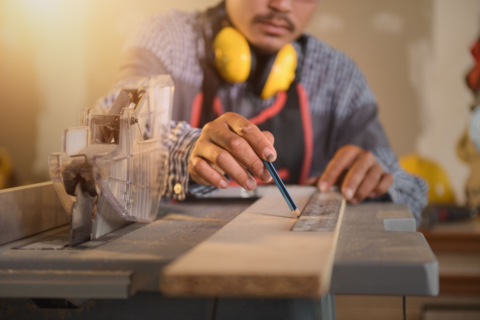 Person using a circular saw to cut wood in a workshop, with safety headphones around the neck Person using a circular saw to cut wood in a workshop, with safety headphones around the neck
