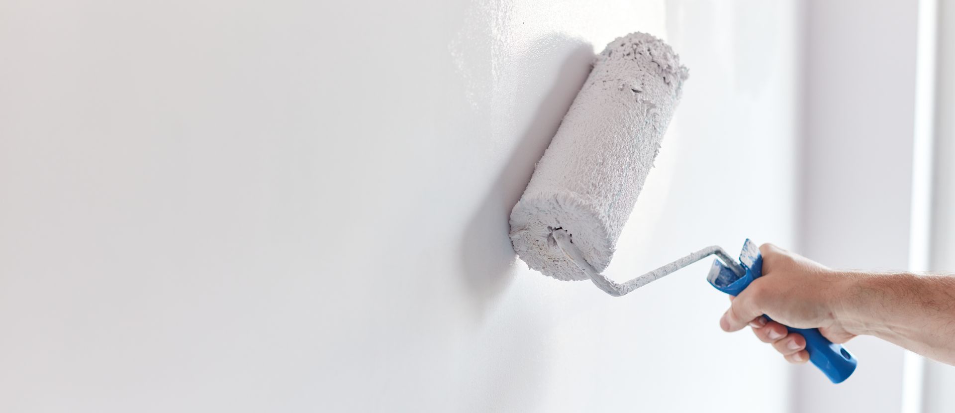 Hand using a paint roller to apply white paint to a wall Hand using a paint roller to apply white paint to a wall