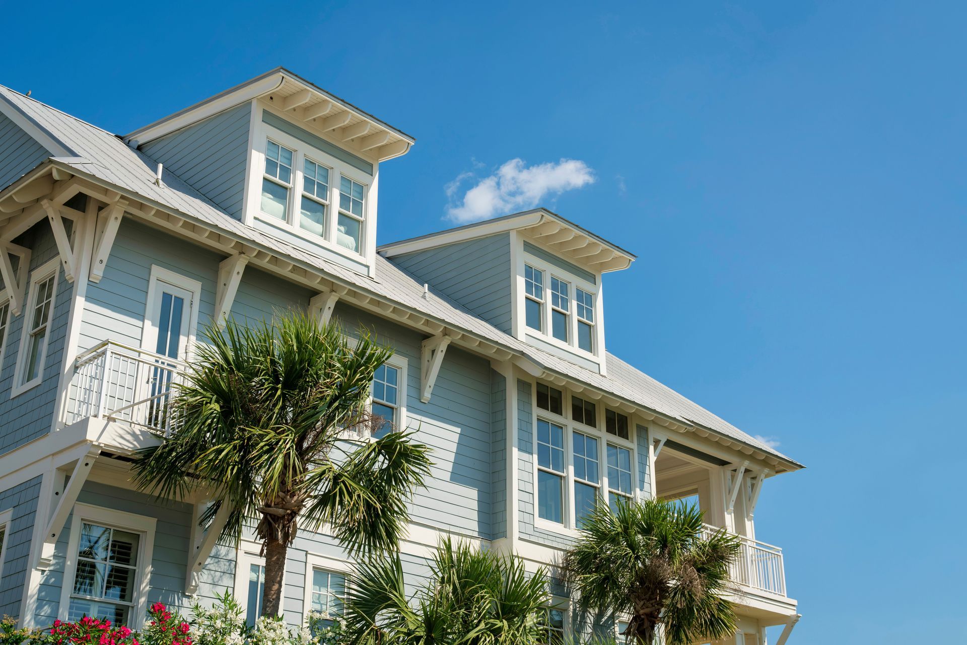 White coastal-style building with balconies and palm trees against a bright blue sky White coastal-style building with balconies and palm trees against a bright blue sky