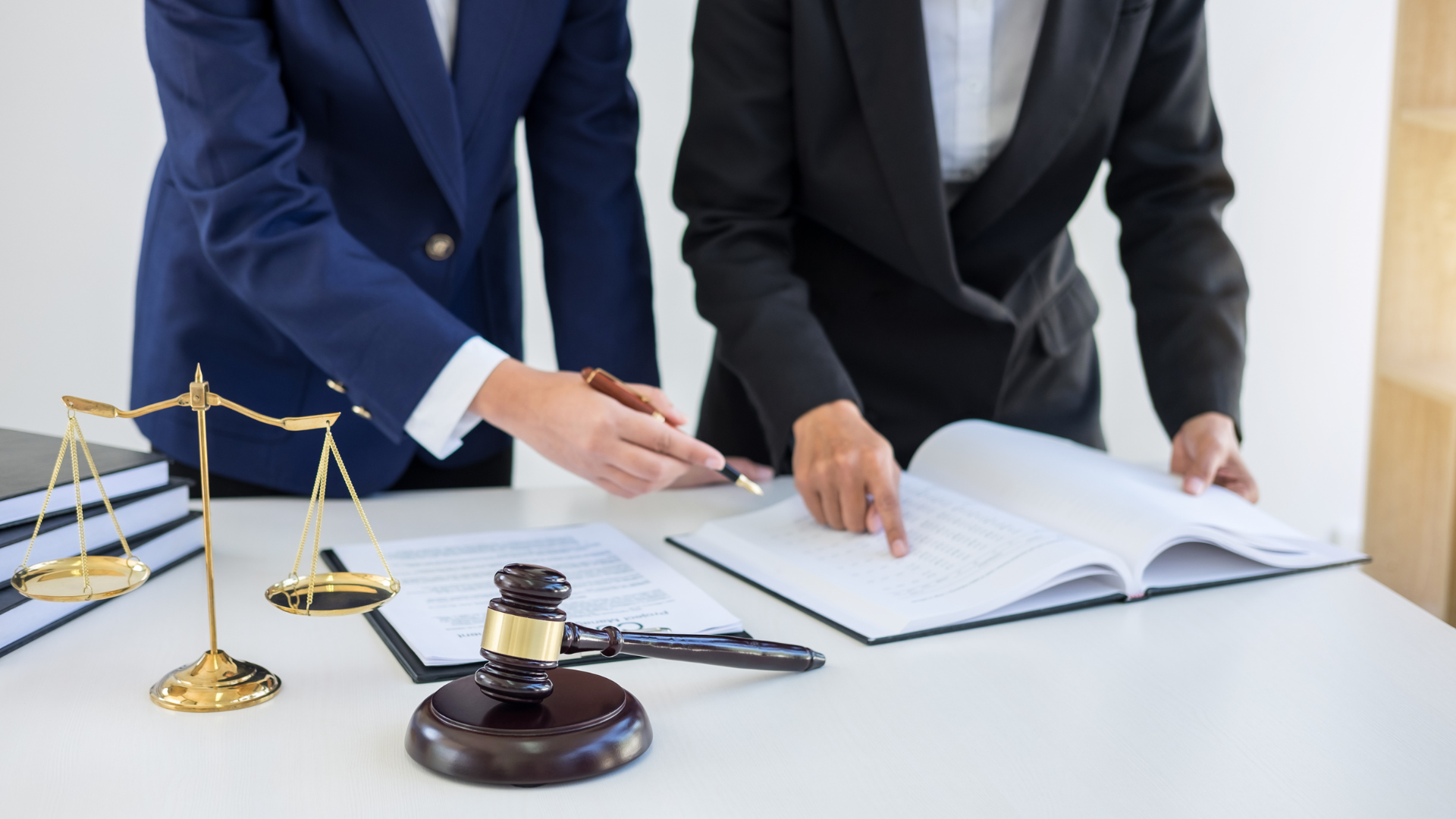 Two businesspeople signing legal documents beside a gavel and scales of justice