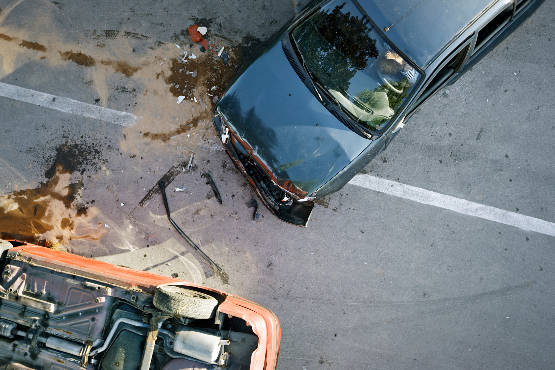 Overhead view of a dark blue car and orange vehicle after a crash, with debris on the road