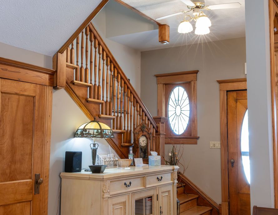 Wooden staircase and entryway with a side table, lamp, window, and ceiling light in a cozy home interior