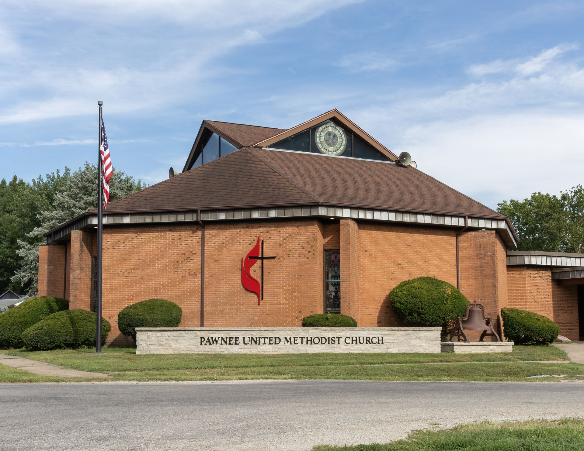 Round brick church building with a red cross sign, American flag, and steeple under a blue sky