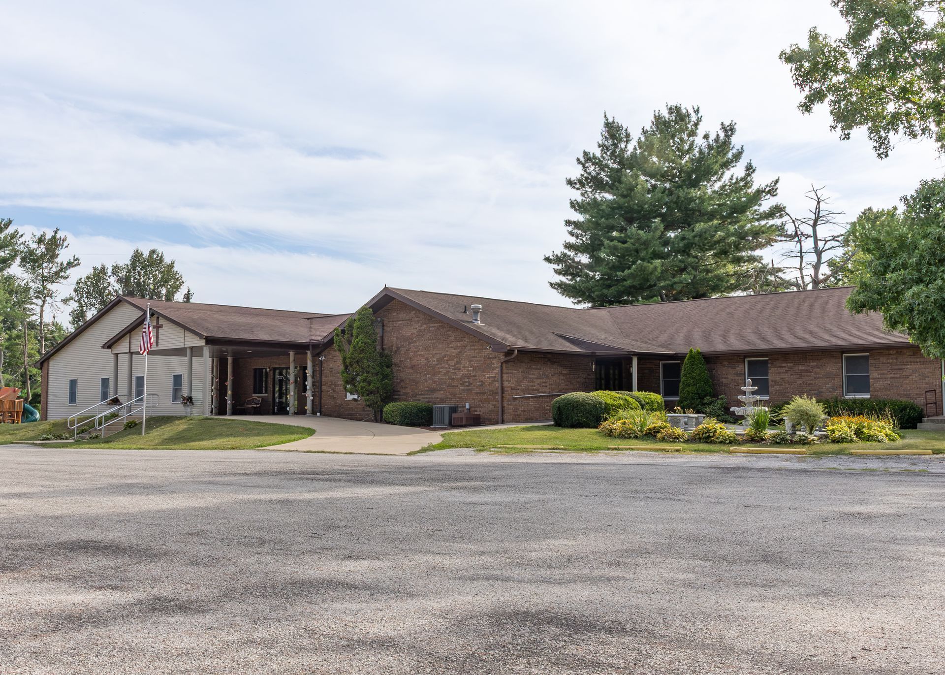 Single-story brick building with a covered entrance and parking lot under a cloudy sky