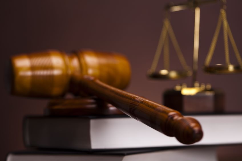 A wooden gavel sitting on top of a book next to a scale of justice