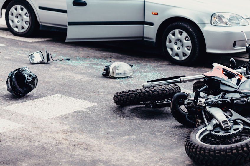 A motorcycle has crashed into a car on the side of the road.