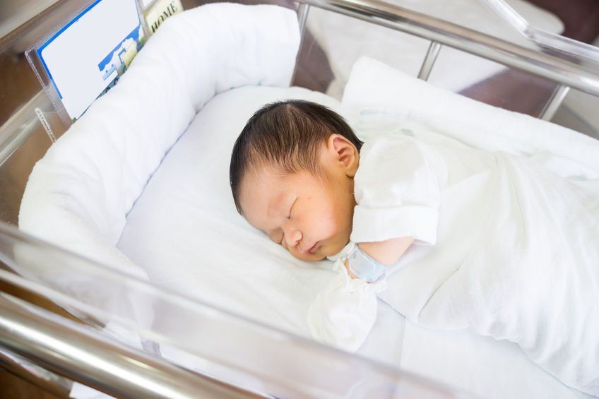 A newborn baby is sleeping in a hospital bed.