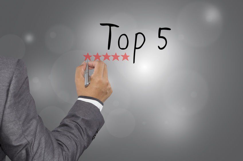 A man in a suit is writing the word top 5 with a marker.