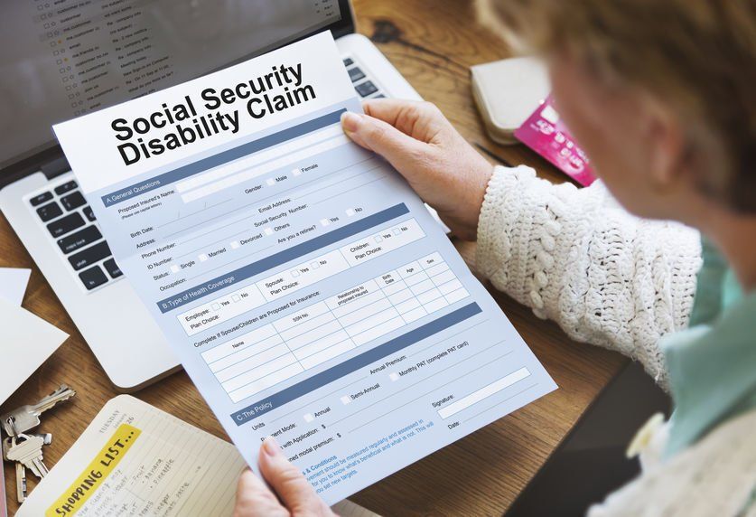 A woman is holding a social security disability claim form in front of a laptop computer.