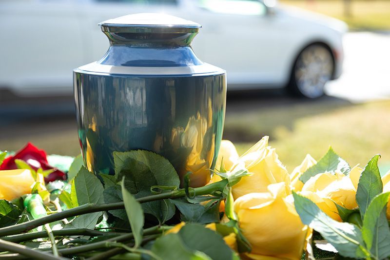 Cremation urn with flowers and hearse in background