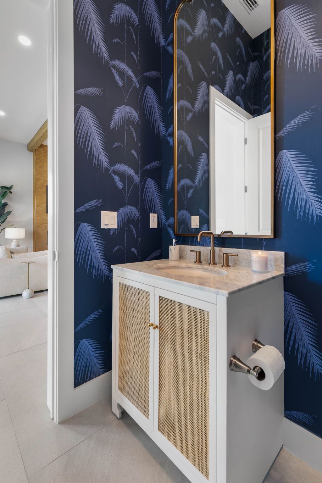 Modern bathroom vanity with navy leaf wallpaper, white cabinet, mirror, and copper fixtures