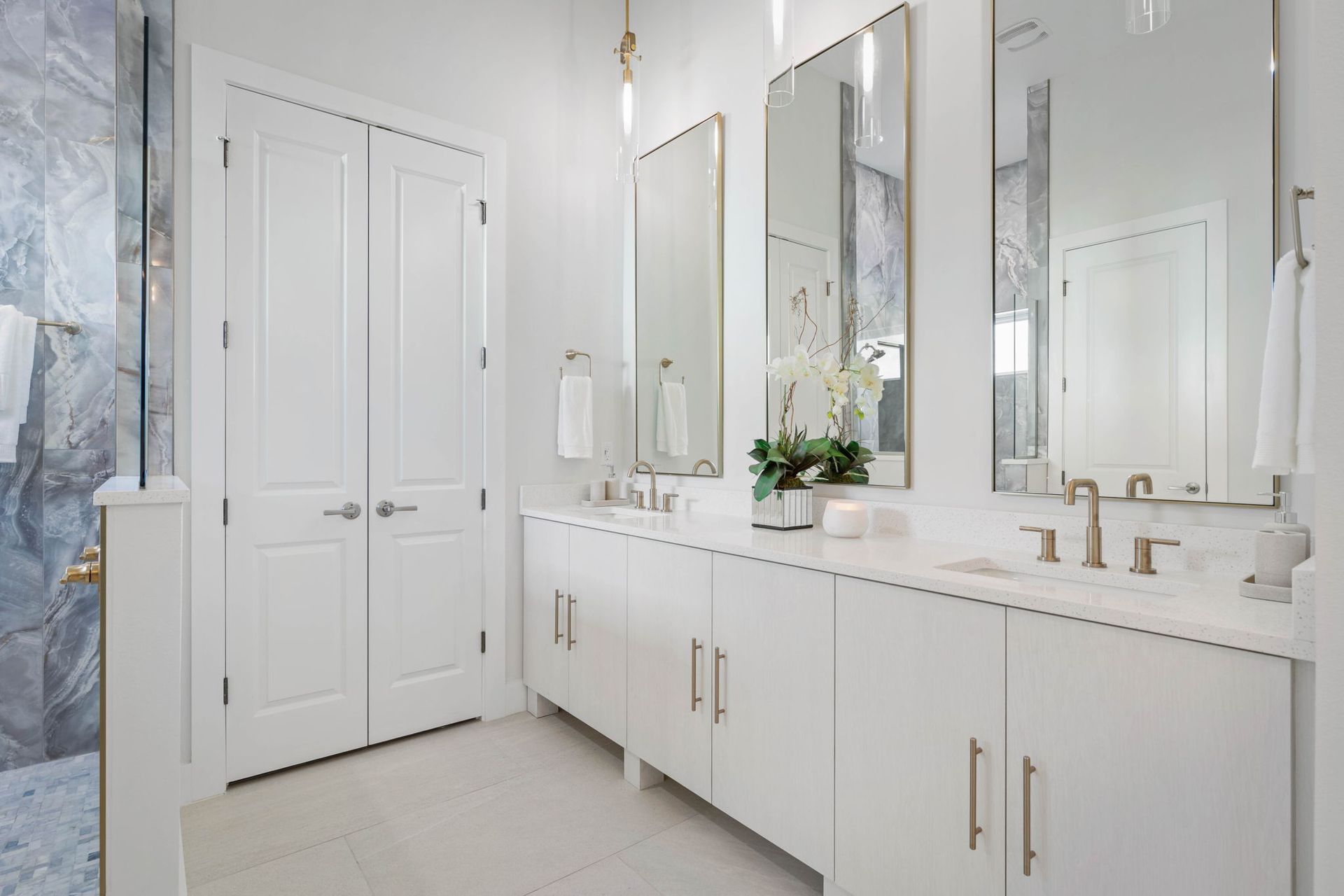 Bright white bathroom with double vanity, large mirrors, and a vase of flowers.