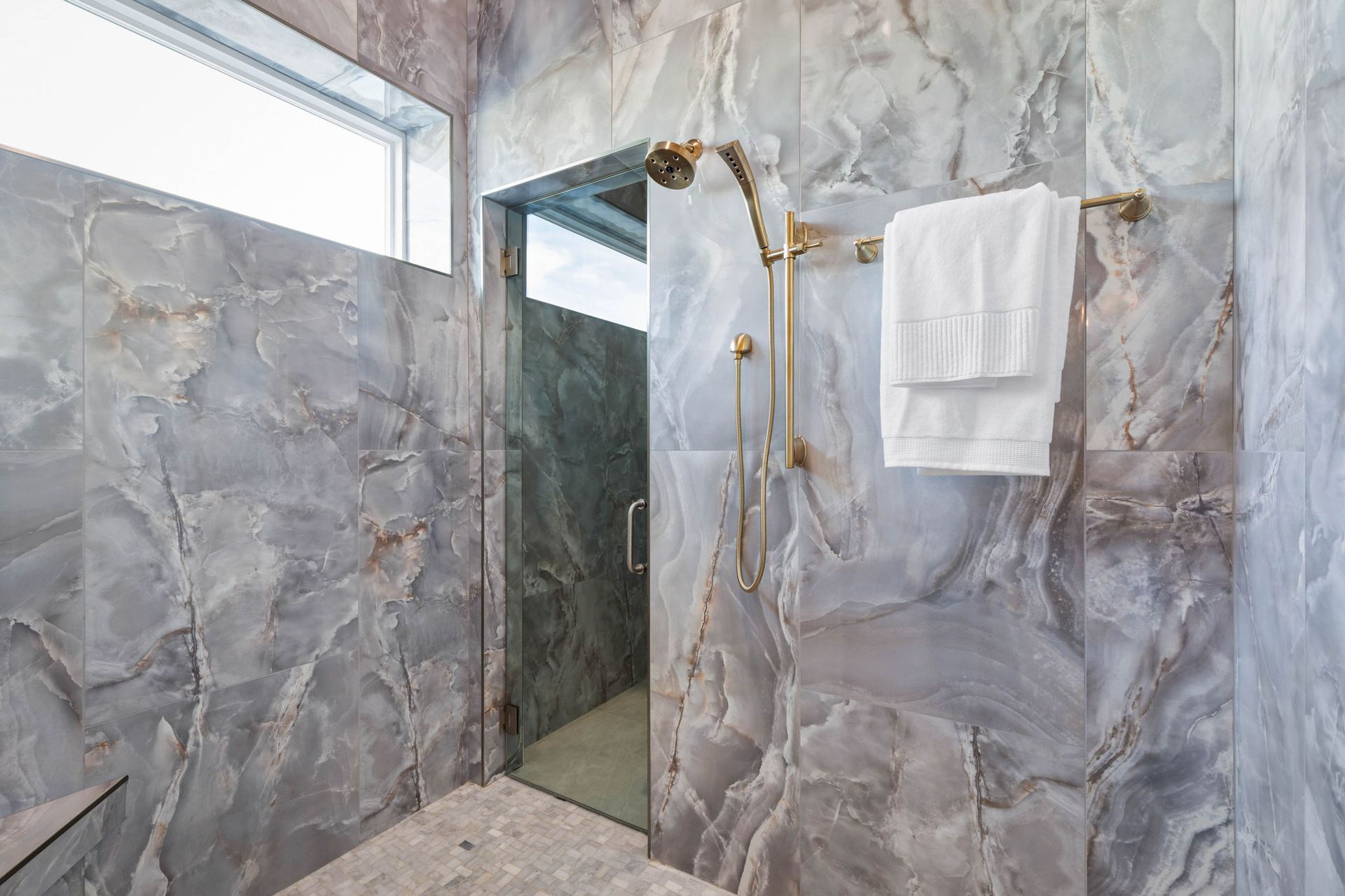 Marble-tiled shower with glass door, gold fixtures, and white towels in a modern bathroom