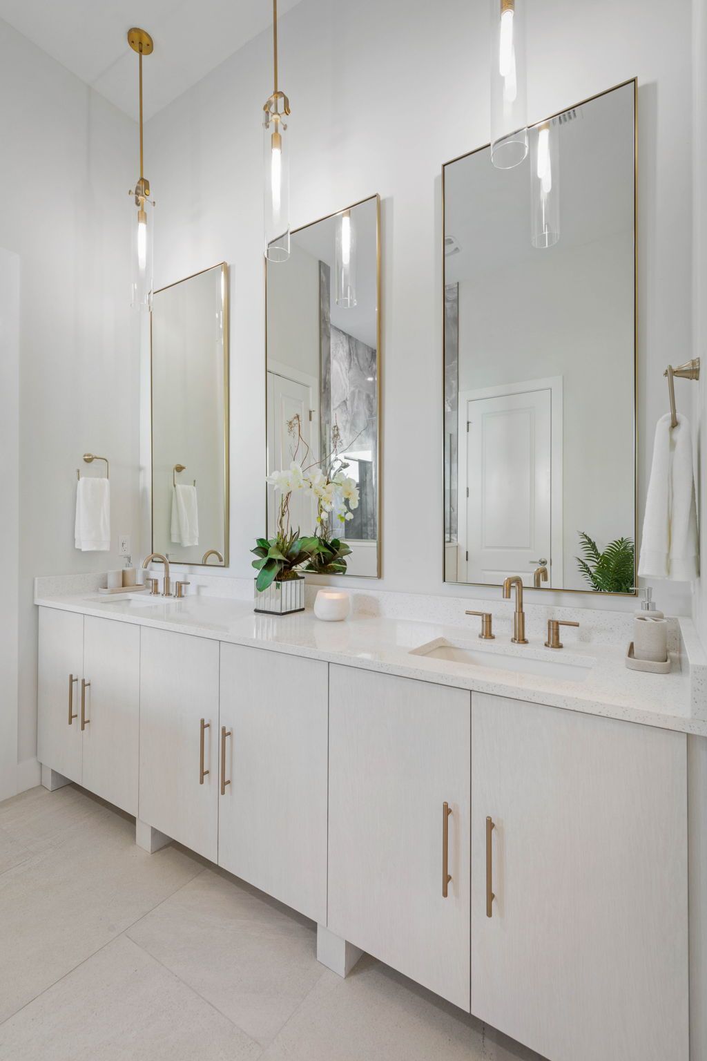 Modern white bathroom vanity with three mirrors, gold fixtures, and a small flower arrangement.