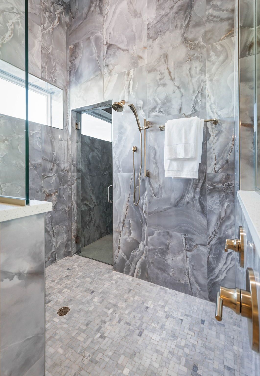 Modern marble-tiled shower with glass door, towel hooks, and brass fixtures.