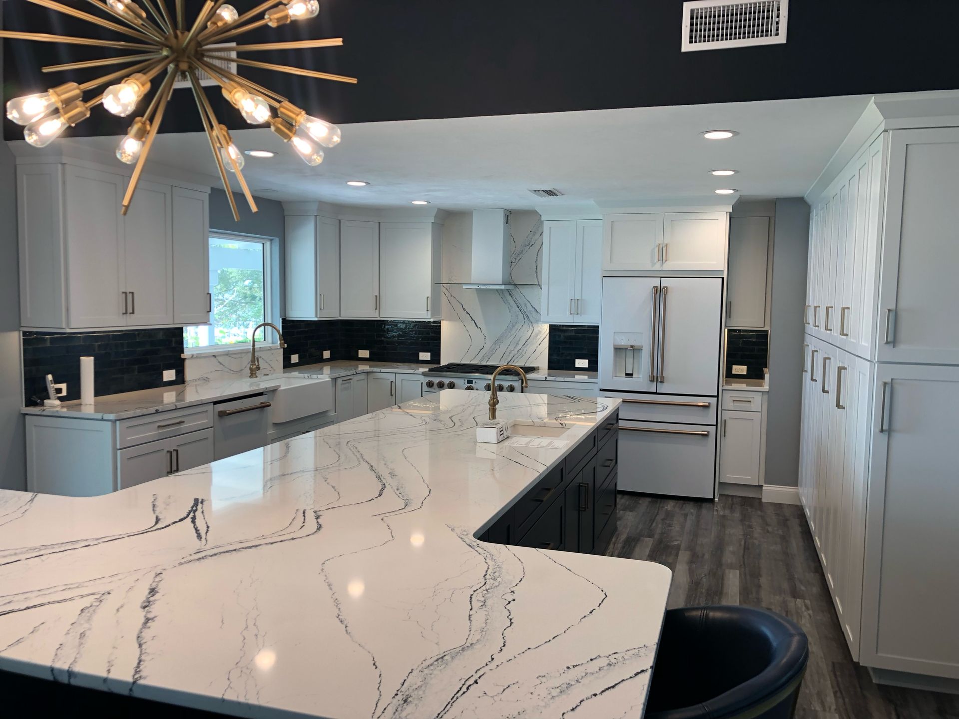 Modern white kitchen with marble island, black accents, and a starburst chandelier