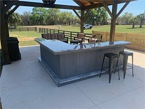Outdoor pavilion with a bar counter and stools overlooking a grassy park