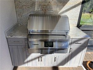 Built-in stainless steel outdoor grill with gray cabinets and granite countertop in a patio nook
