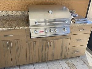 Stainless steel gas grill built into a wood cabinet outdoors on a patio.