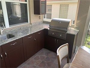 Outdoor patio kitchen with dark cabinets, granite countertop, sink, and stainless grill under a covered area
