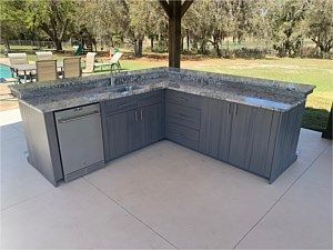 Outdoor L-shaped gray granite kitchen island with built-in grill on a patio