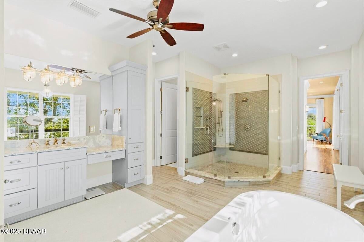 Bright bathroom with double vanity, walk-in shower, soaking tub, and ceiling fan in white and beige tones