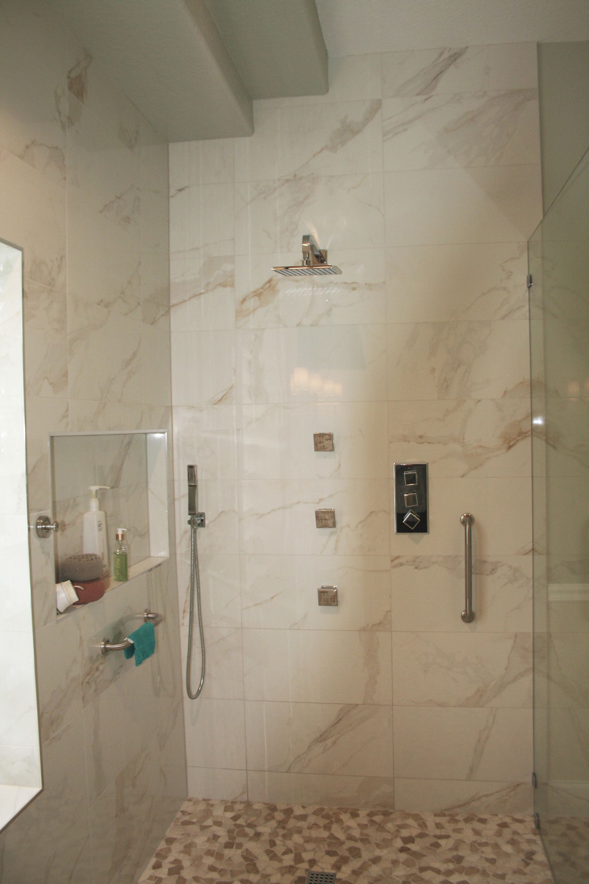 Modern tiled shower with glass door, grab bars, handheld shower, and mosaic floor.