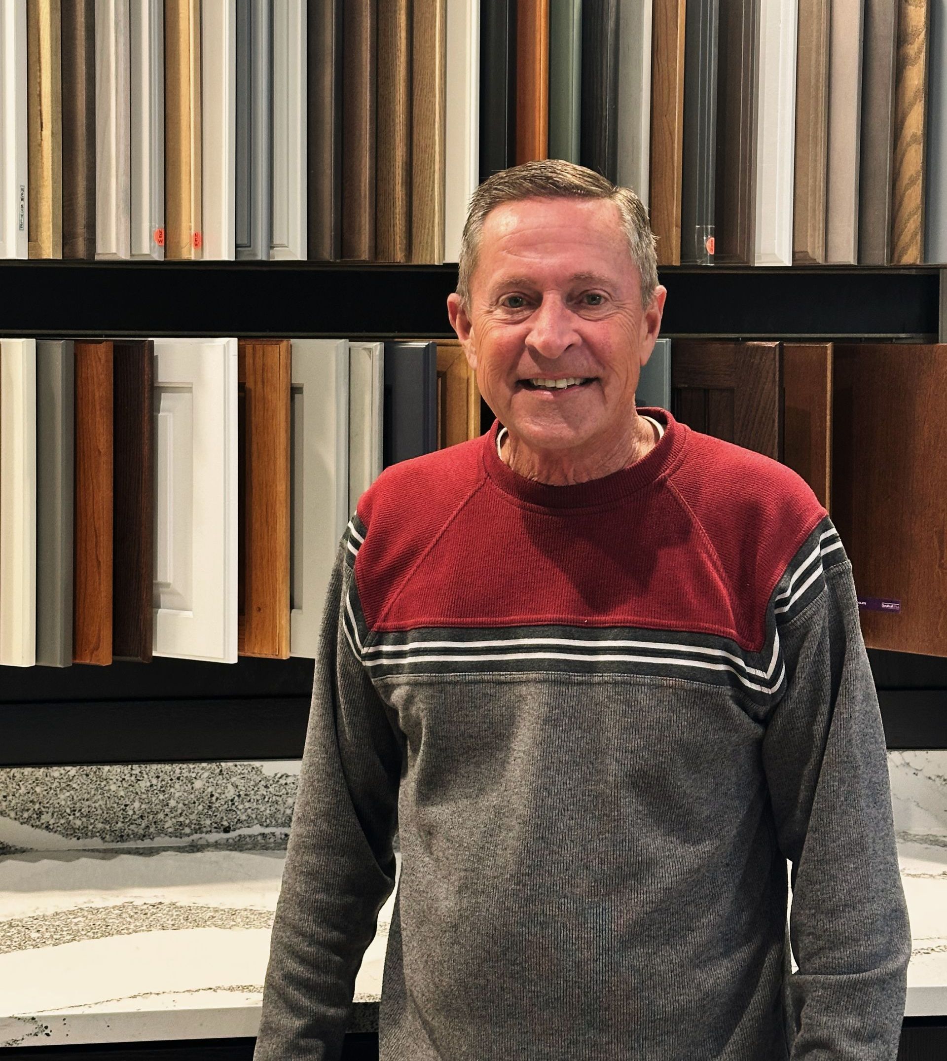 Smiling person in a red and gray sweater standing before shelves of rolled fabric samples