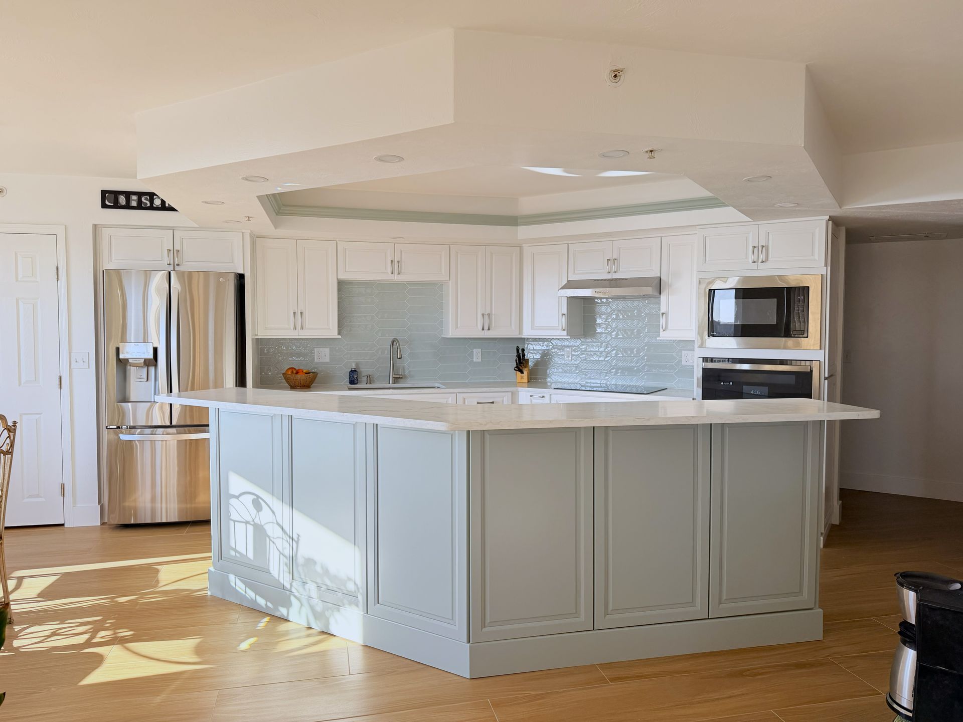 Bright white kitchen with island, stainless steel fridge, microwave, and marble countertops
