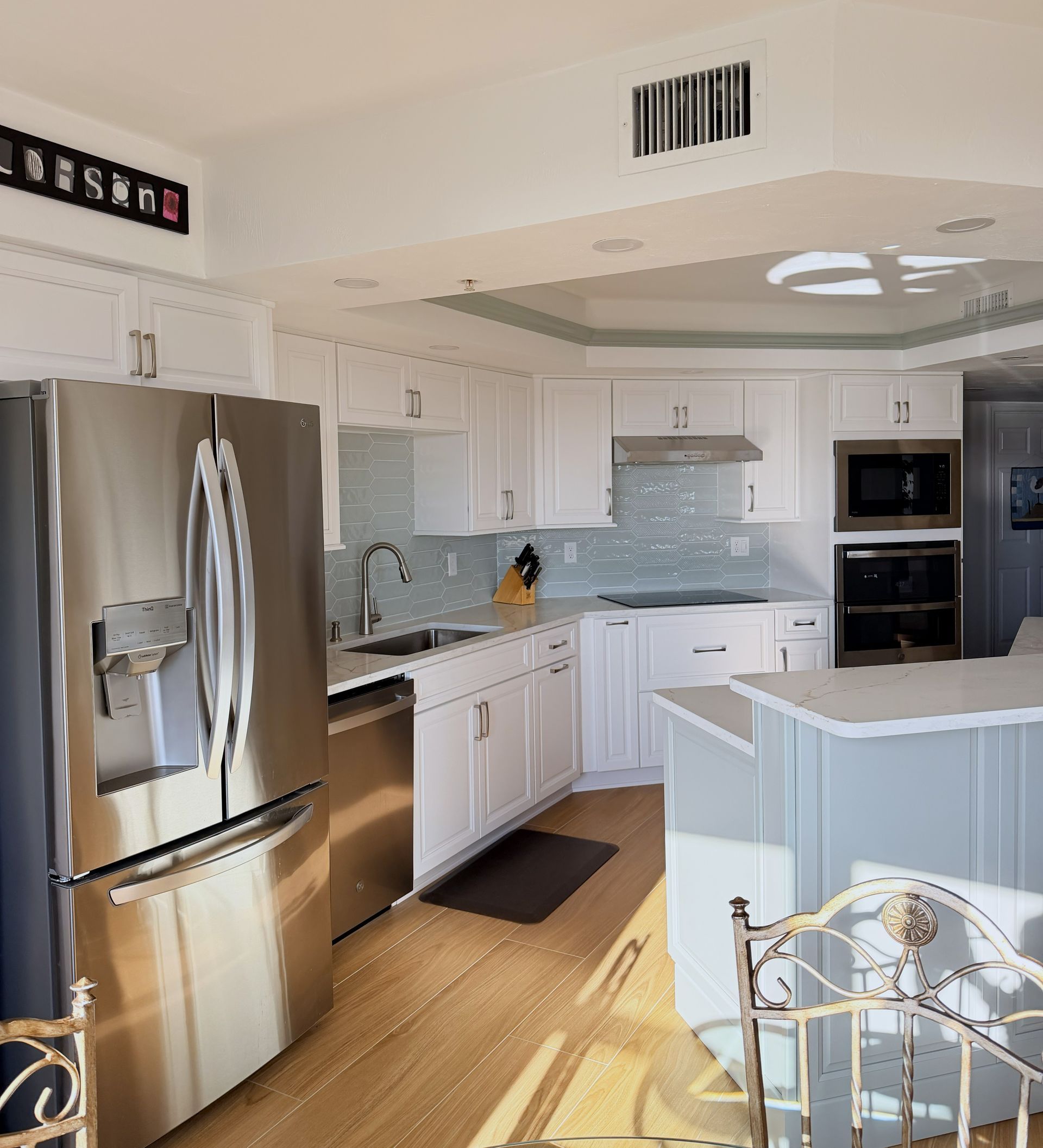 Bright white kitchen with stainless steel appliances, island, marble counters, and sunlit wood floor