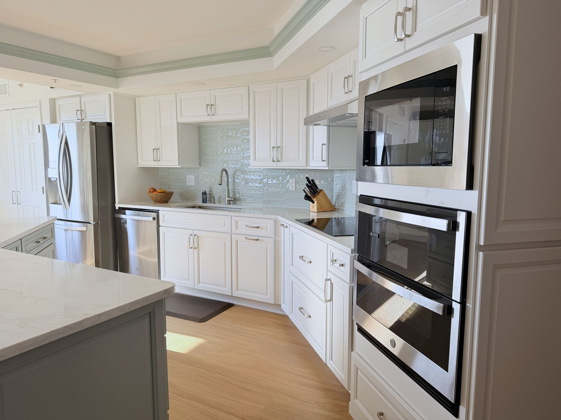 Bright white kitchen with stainless steel appliances, wood floor, and built-in double ovens