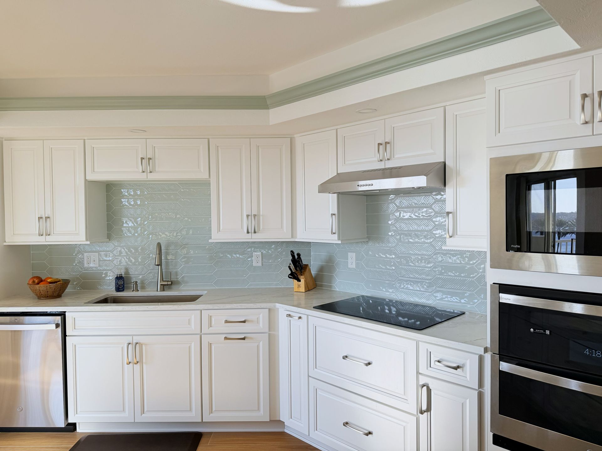 Bright white modern kitchen with cabinets, mosaic backsplash, and stainless steel appliances.