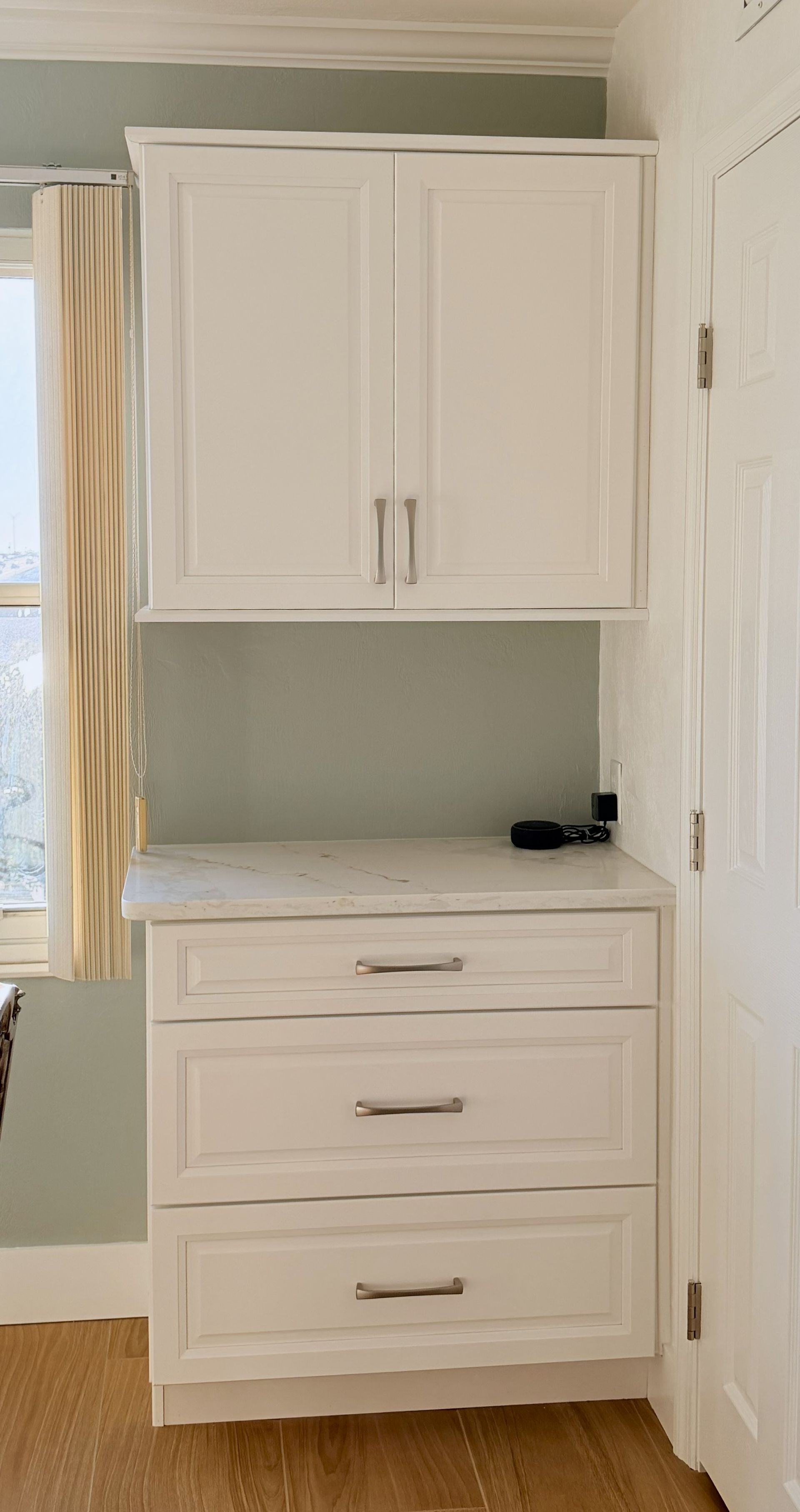 White built-in cabinet with upper doors and three drawers in a light green room.