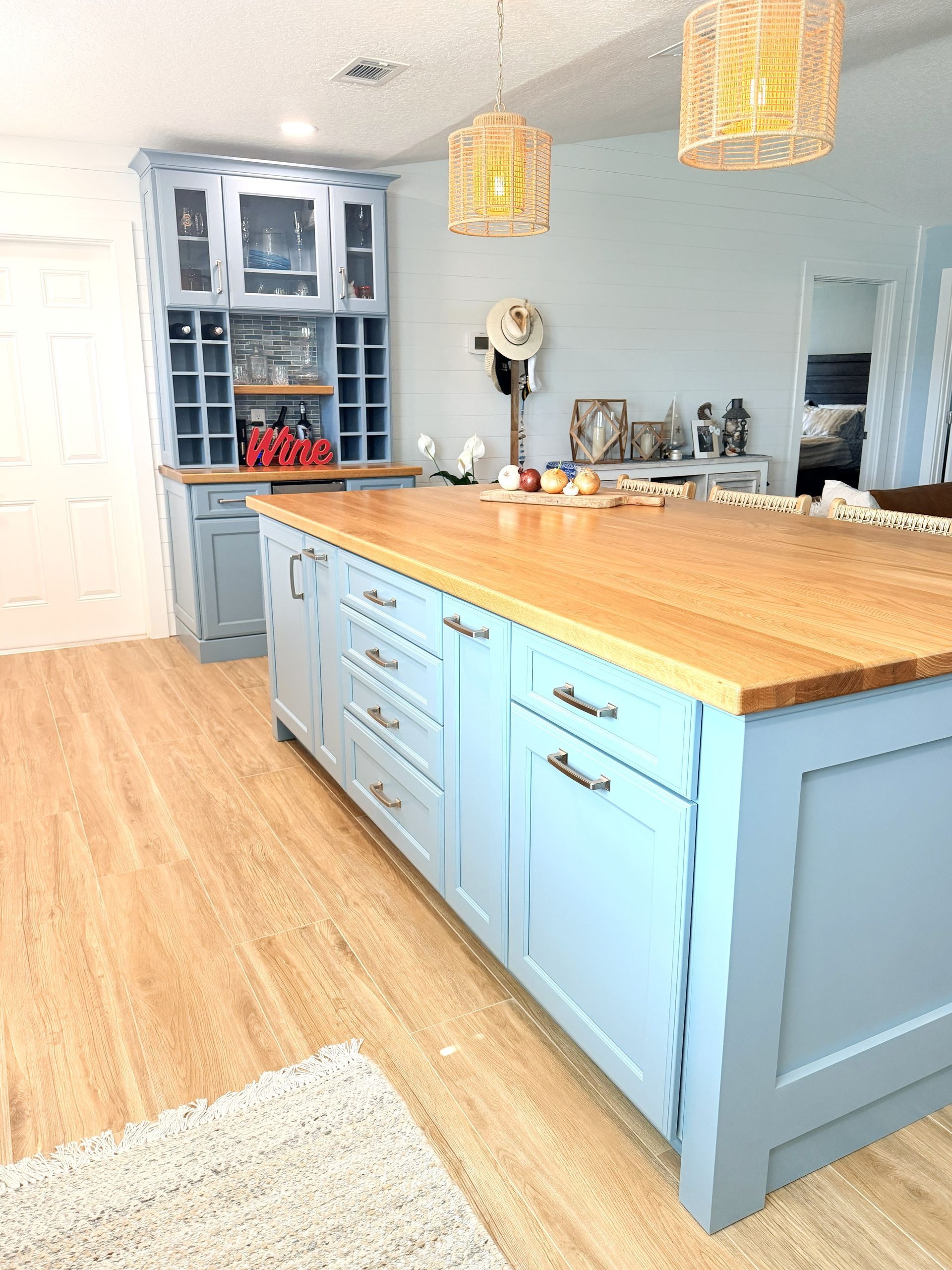 Bright kitchen with blue cabinets, wooden island, and pendant lights on a light wood floor.