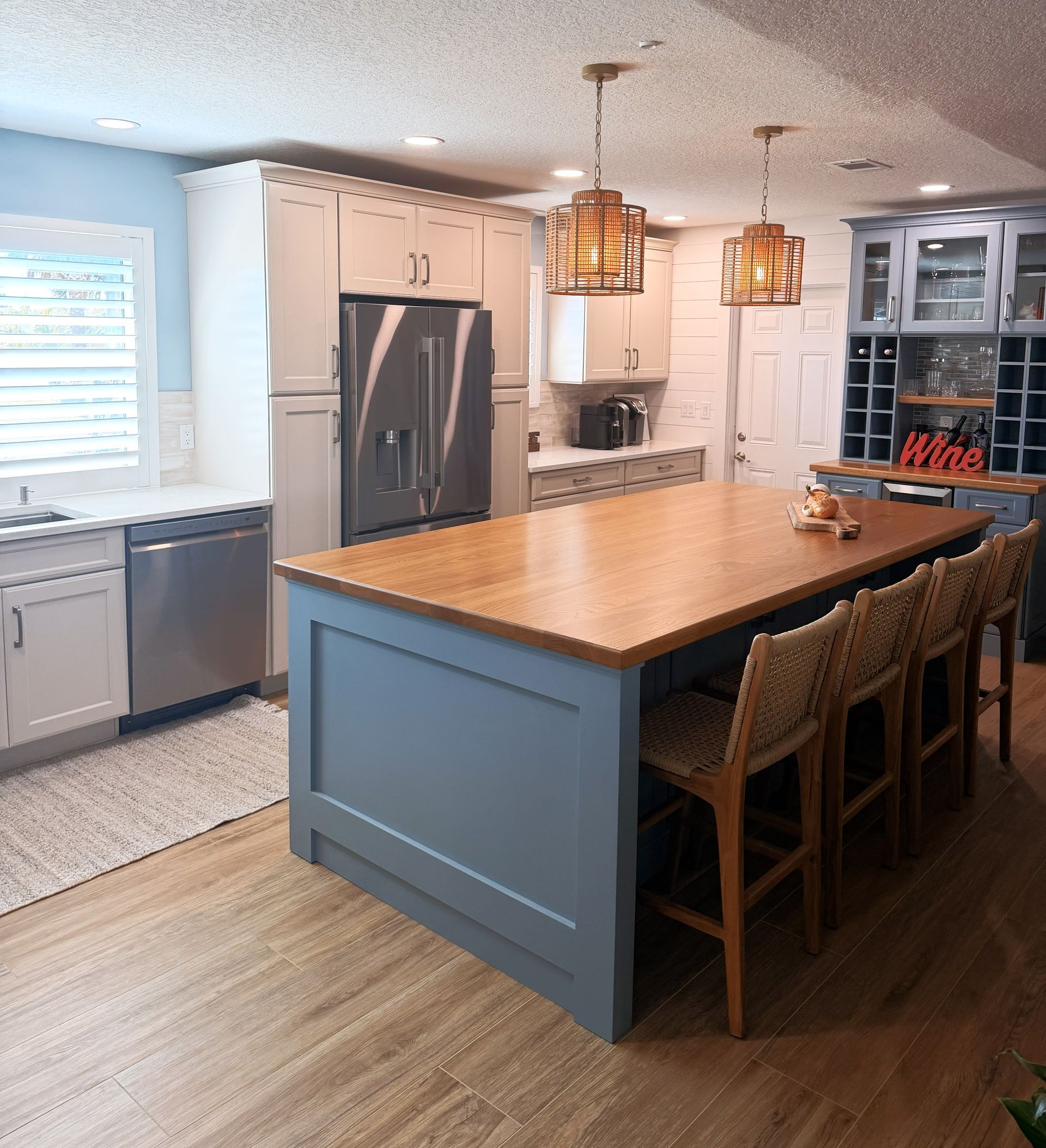 Bright kitchen with a large wood island, gray cabinets, pendant lights, and stainless steel appliances.