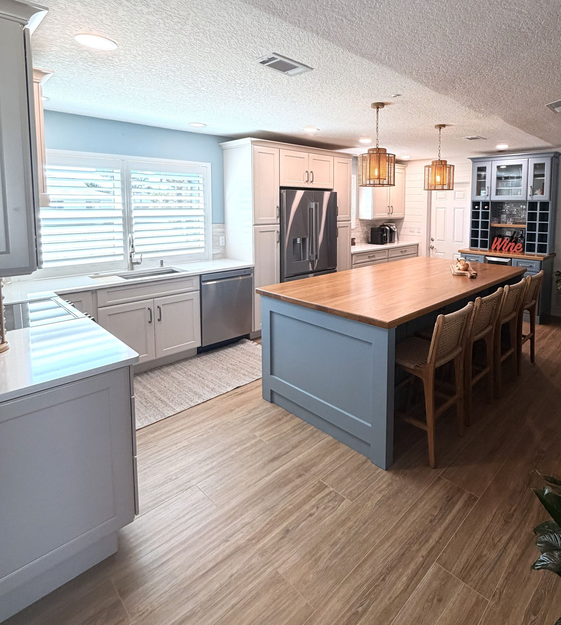 Bright modern kitchen with blue island, wood floors, white cabinets, and a sink under a window