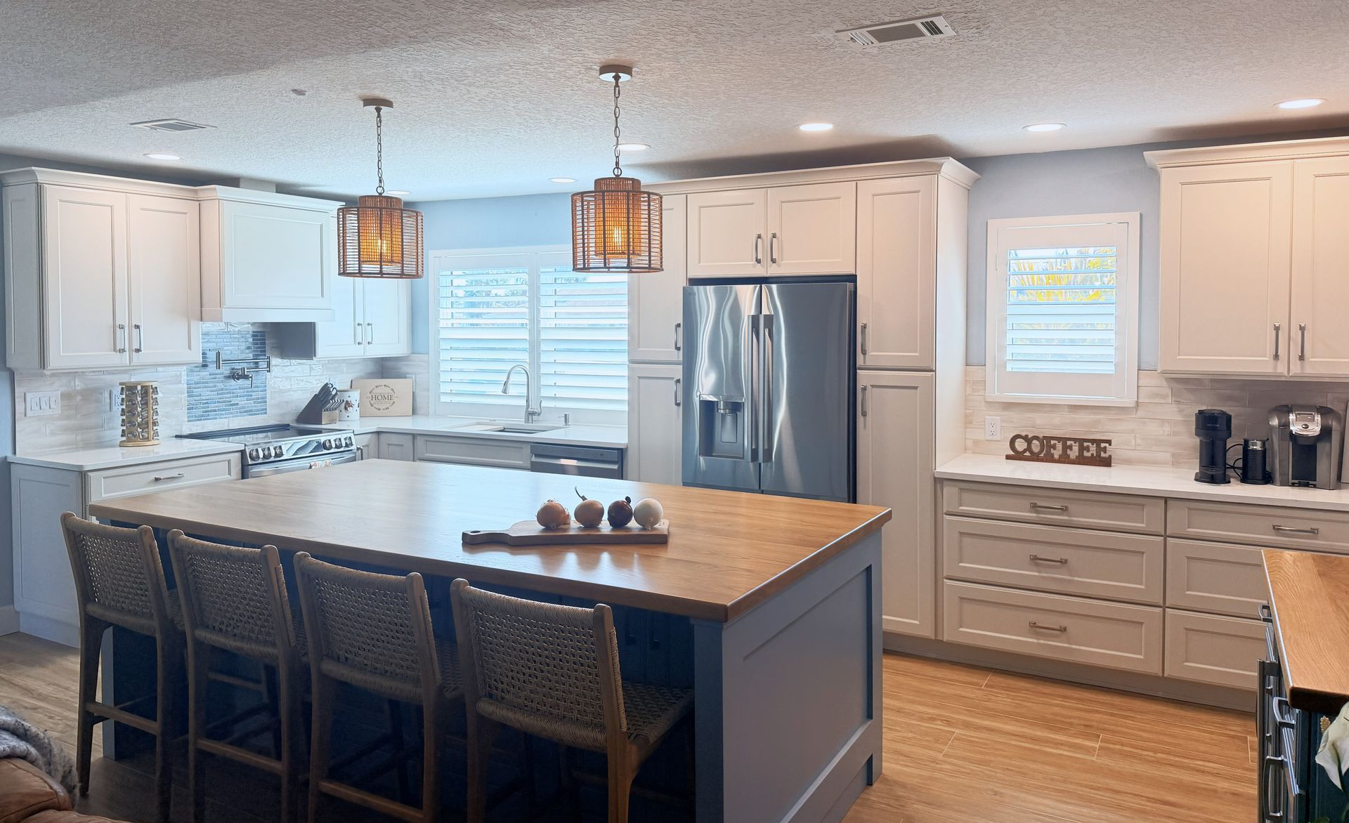 Bright modern kitchen with island, pendant lights, stainless fridge, white cabinets, and wood floors.